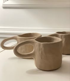 three coffee mugs sitting on top of a white table next to each other in front of a mirror