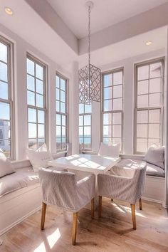 a dining room table with chairs and windows overlooking the ocean in front of them is surrounded by white couches