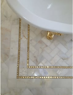 a white sink sitting on top of a marble floor next to a bathtub with gold trim