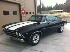 an old black car parked in front of a garage