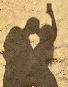 a shadow of a person holding a cell phone up in the air with one hand