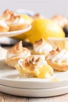 lemon meringue tarts on a plate with other desserts in the background