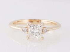 a yellow gold ring with a princess cut diamond and three small diamonds on the band