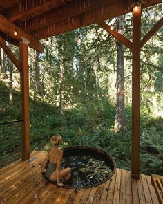 a woman sitting in a hot tub on top of a wooden deck next to trees