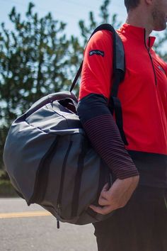 a man carrying a duffel bag while walking down the street with trees in the background