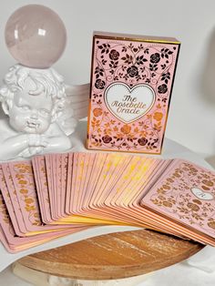 pink and gold playing cards sitting on top of a wooden table next to a statue