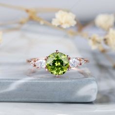 a green and white ring sitting on top of a marble slab with flowers in the background