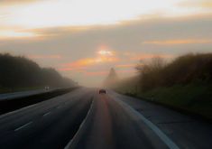 a car driving down the road on a foggy day with sun peeking through the clouds