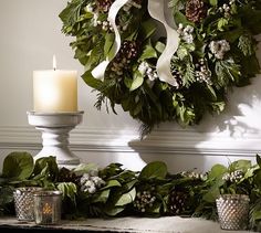 a wreath and candles on a mantle with greenery