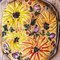 a pie decorated with fruit and vegetables on top of a wooden table next to a knife