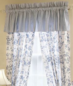 a window with blue and white curtains hanging on it's side, next to a lamp