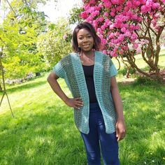 a woman standing in the grass with her hands on her hips, wearing a green crocheted cardigan