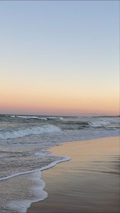 an ocean beach with waves coming in to shore and the sun setting on the horizon