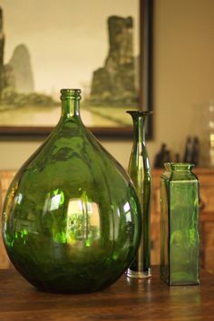 three green vases sitting on top of a wooden table in front of a painting