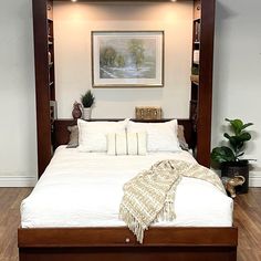 a bed with white linens and pillows in a room that has hardwood floors, a painting on the wall