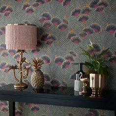 two pineapples on a table next to a lamp and other items in front of a wallpaper