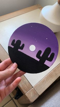 a person holding up a purple and black sticker with cacti on it