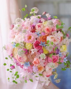 a bridal bouquet with pink, yellow and blue flowers in front of a window