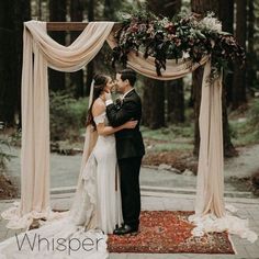 a bride and groom kissing under an outdoor wedding ceremony arch with draping over it