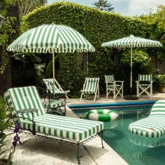 two lawn chairs sitting next to a swimming pool with umbrellas on top of it