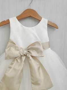 a white dress with a large bow on the front and back, hanging on a wooden hanger