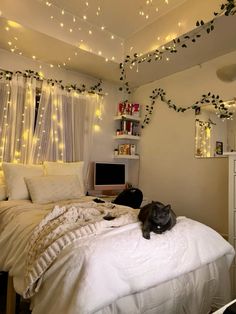 a cat laying on top of a white bed in a room with fairy lights hanging from the ceiling