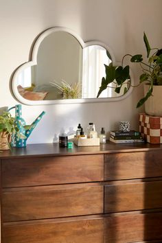 a wooden dresser topped with lots of clutter next to a mirror and potted plant