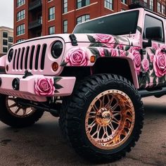 a pink jeep with roses painted on it's side and gold rims is parked in front of a brick building