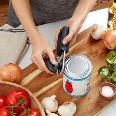 a person using a can opener on a cutting board next to some vegetables and garlic