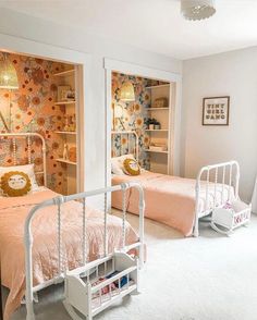 two twin beds in a bedroom with floral wallpaper and white bedding, one has a pink comforter on it