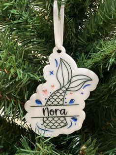 a white ornament hanging from a tree with the word nora on it