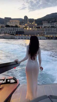 a woman in a white dress standing on the back of a boat