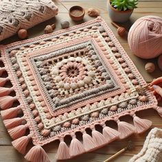 a crocheted square with tassels and yarn next to it on a wooden surface