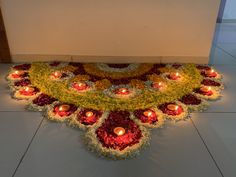 an arrangement of flowers and lit candles on the floor in front of a wall,