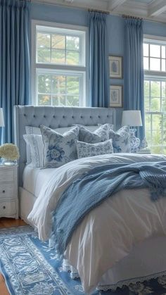 a bedroom with blue walls and white bedding, rugs on the floor and windows