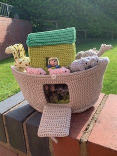 a crocheted basket filled with stuffed animals on top of a brick wall next to grass