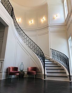 an elegant staircase with two chairs and a vase on the floor