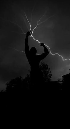 a man is holding his arm up in the air while lightning strikes behind him