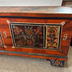 an old wooden chest with floral designs painted on the front and sides, sitting on carpeted floor