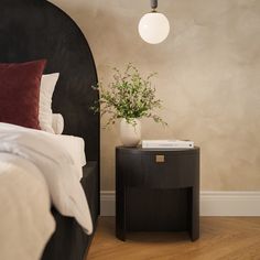 a bed room with a neatly made bed and a plant on the end table next to it