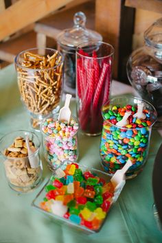 there are many different types of candies on the table and in glass containers with spoons