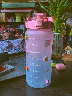 a pink water bottle sitting on top of a wooden table next to a laptop computer