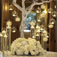 a centerpiece with flowers and candles is displayed in front of a tree decorated with glass globes