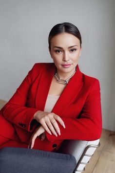 a woman in a red suit is sitting on a chair and posing for the camera