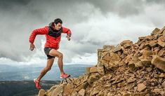 a man running on top of a rocky mountain with storm clouds in the sky behind him