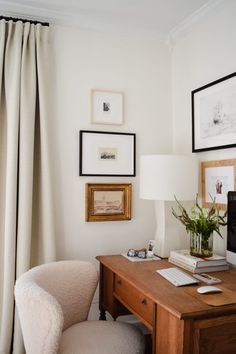 a desk with a computer on top of it next to a chair and framed pictures