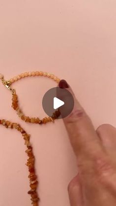 a person pointing to a beaded necklace on a pink surface with a gold chain