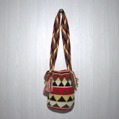 a multicolored bag hanging on a white wall with a tasselled handle