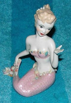 a ceramic figurine of a mermaid sitting on a blue surface with her arms outstretched