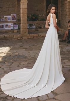 a woman in a white wedding dress standing on a stone walkway with her back to the camera